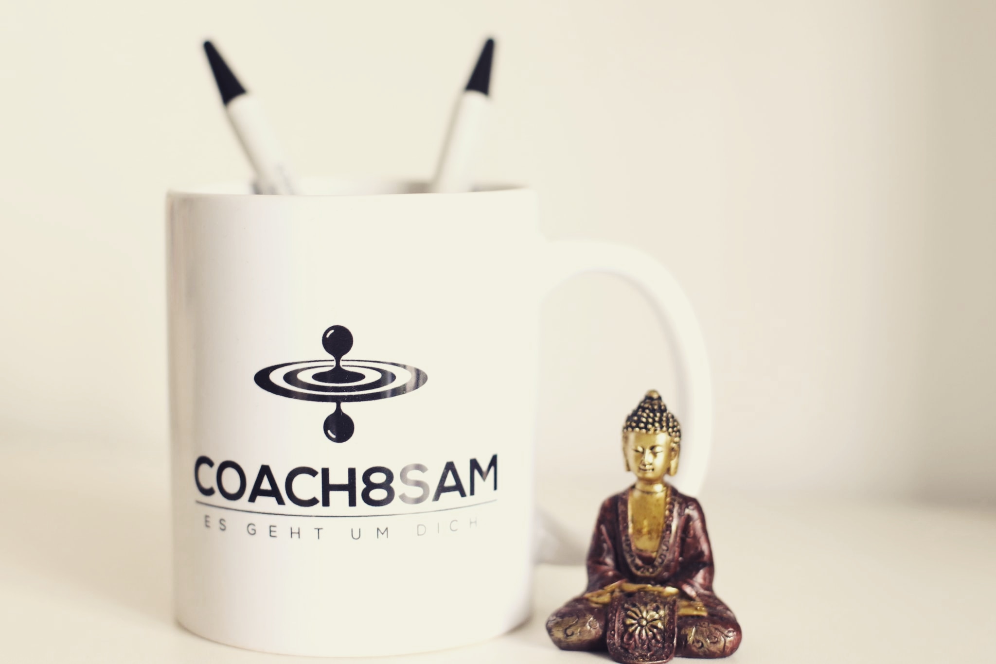 Tasse mit Aufschrift Coach8Sam und kleinem sitzenden Buddha daneben